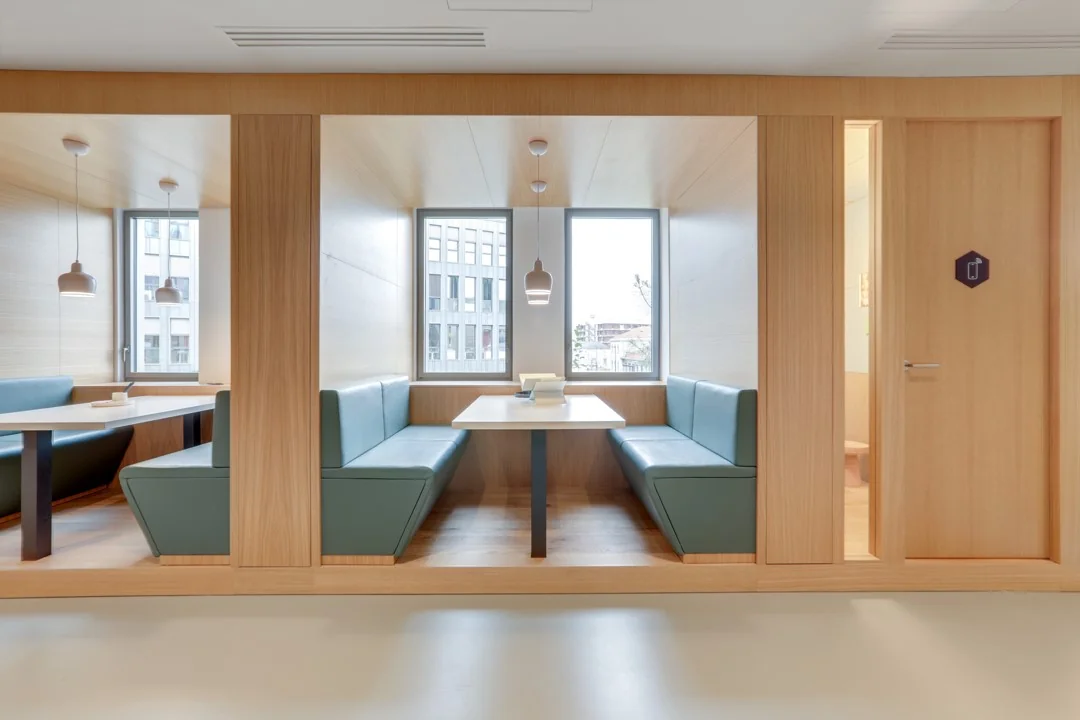 Modern ingerichte zithoek met houten wanden, groenblauwe banken en grote ramen in een kantoorruimte aan de Hoogstraat 1001.