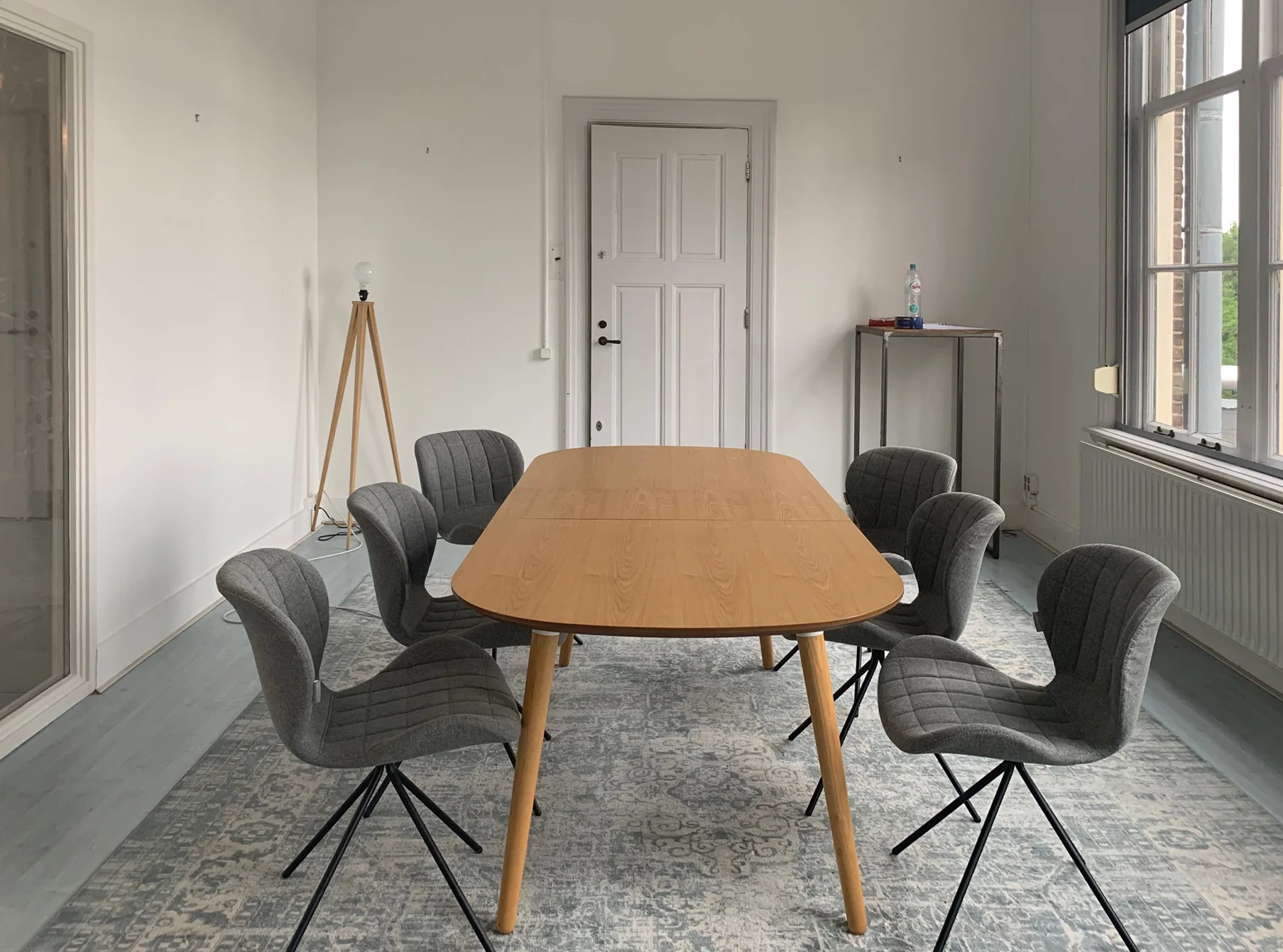 Een moderne vergaderruimte met een houten tafel omringd door zes grijze stoelen.
