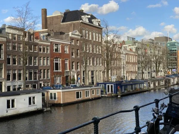 Rij grachtenpanden en woonboten langs een kanaal op een zonnige dag in Amsterdam.