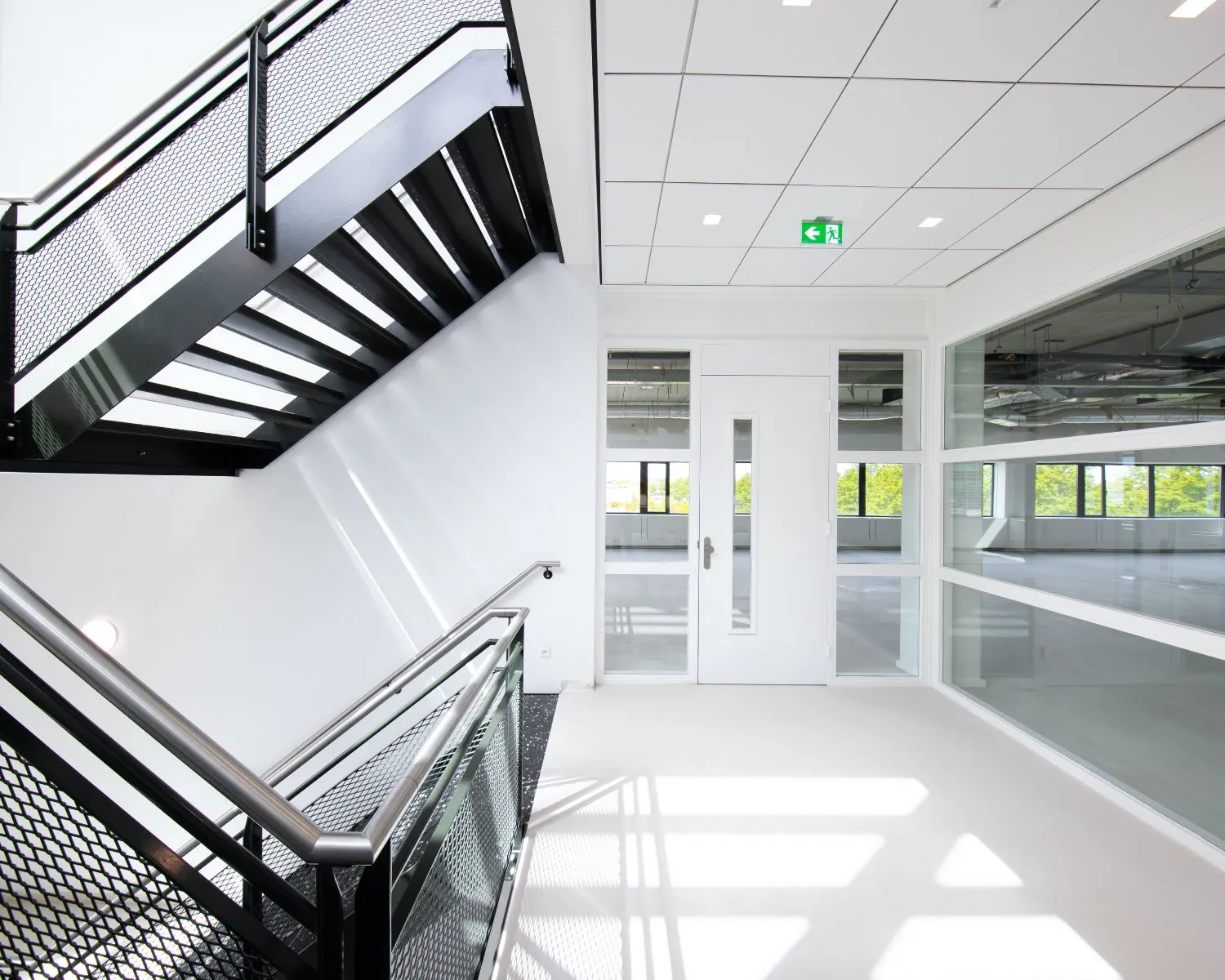 Moderne, lichte kantoorruimte met witte muren, grote ramen en een zwart metalen trap in het pand aan de Basicweg 12 in Amersfoort.