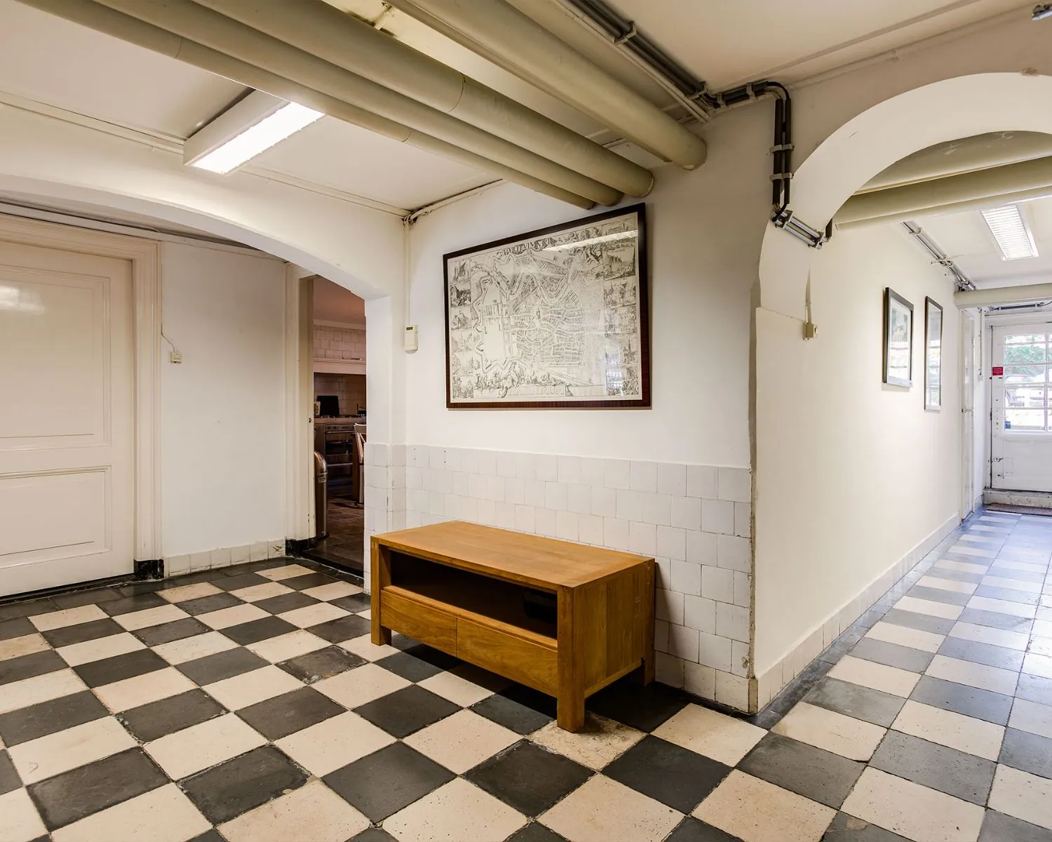 Hal van kantoorruimte aan de Dreef 36 in Haarlem met zwart-wit geblokte tegelvloer, houten tafeltje en wanddecoratie.