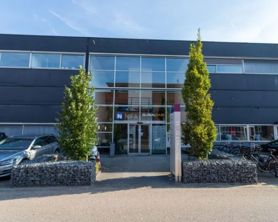 Vooraanzicht van een modern kantoorpand aan de Fruitweg 22-24 met glasgevel en bedrijfsnaambord "NIFA Global Hair".