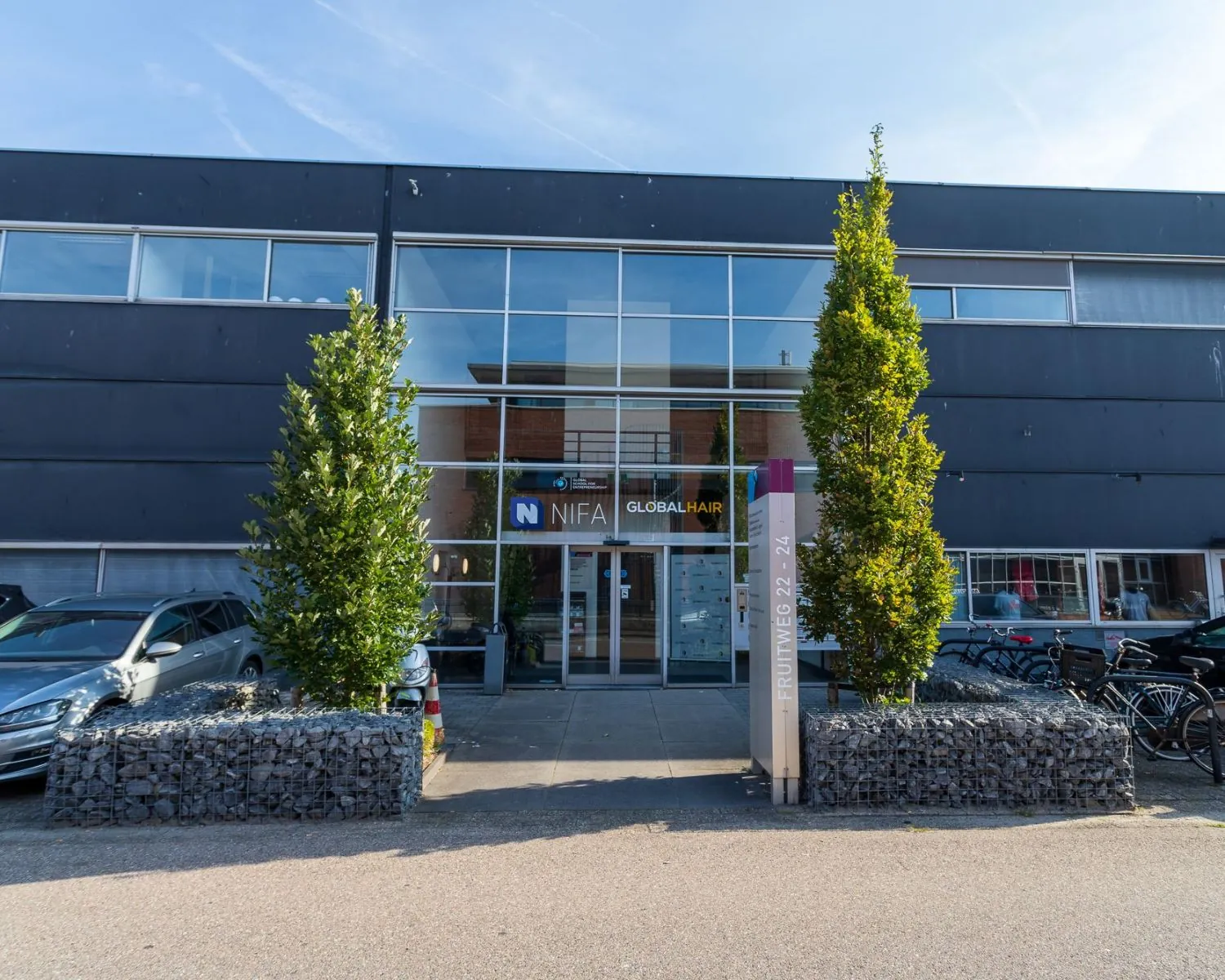 Vooraanzicht van een modern kantoorpand aan de Fruitweg 22-24 met glasgevel en bedrijfsnaambord "NIFA Global Hair".