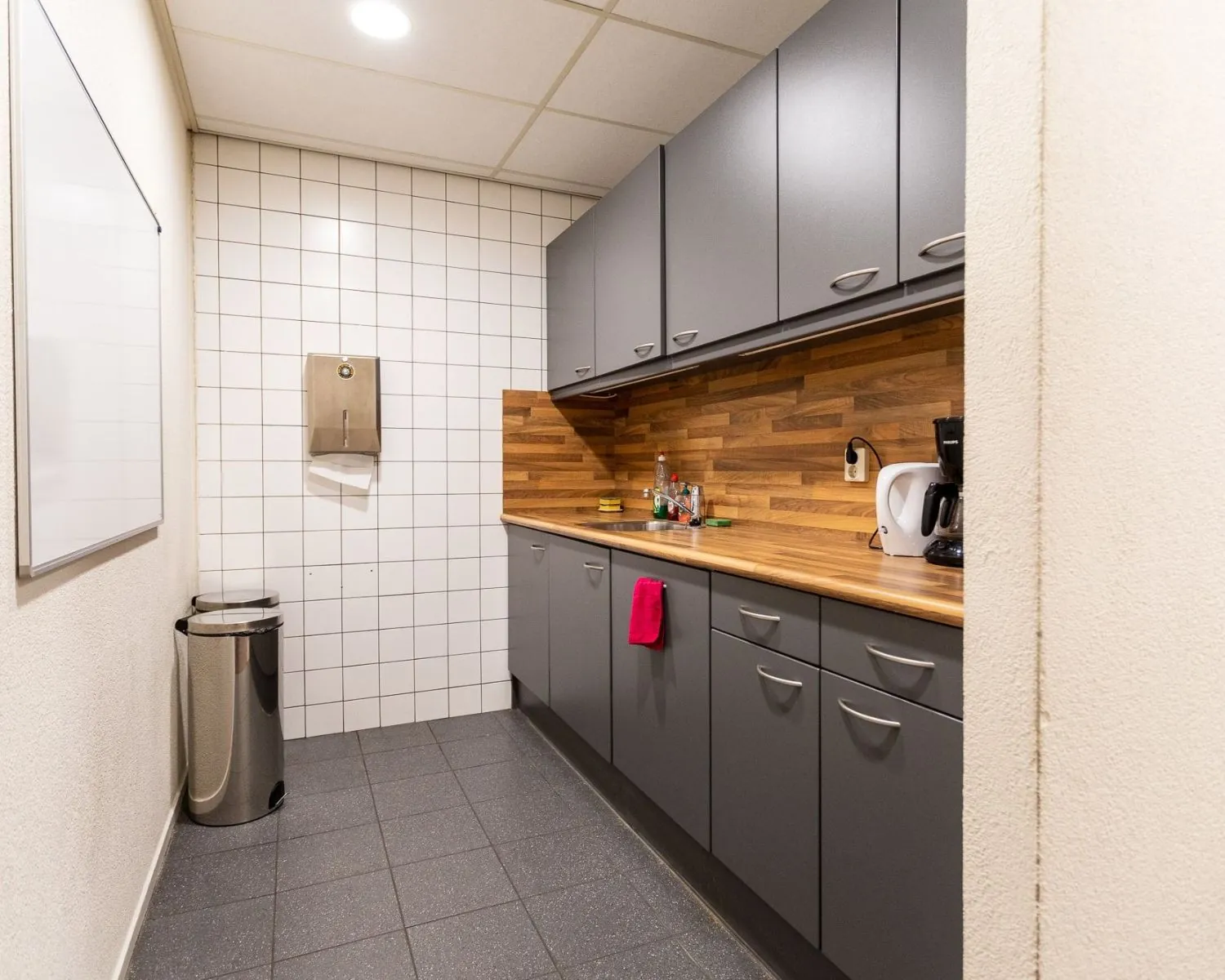 Keukenblok in een kantoorruimte met grijze kasten, houten aanrechtblad en witte tegelwand aan de Fruitweg 16-30.