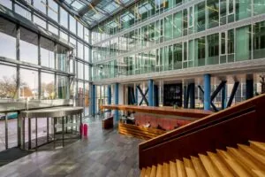 Moderne entreehal van Kennedy Tower in Eindhoven met glazen gevel, houten trap en receptiebalie.