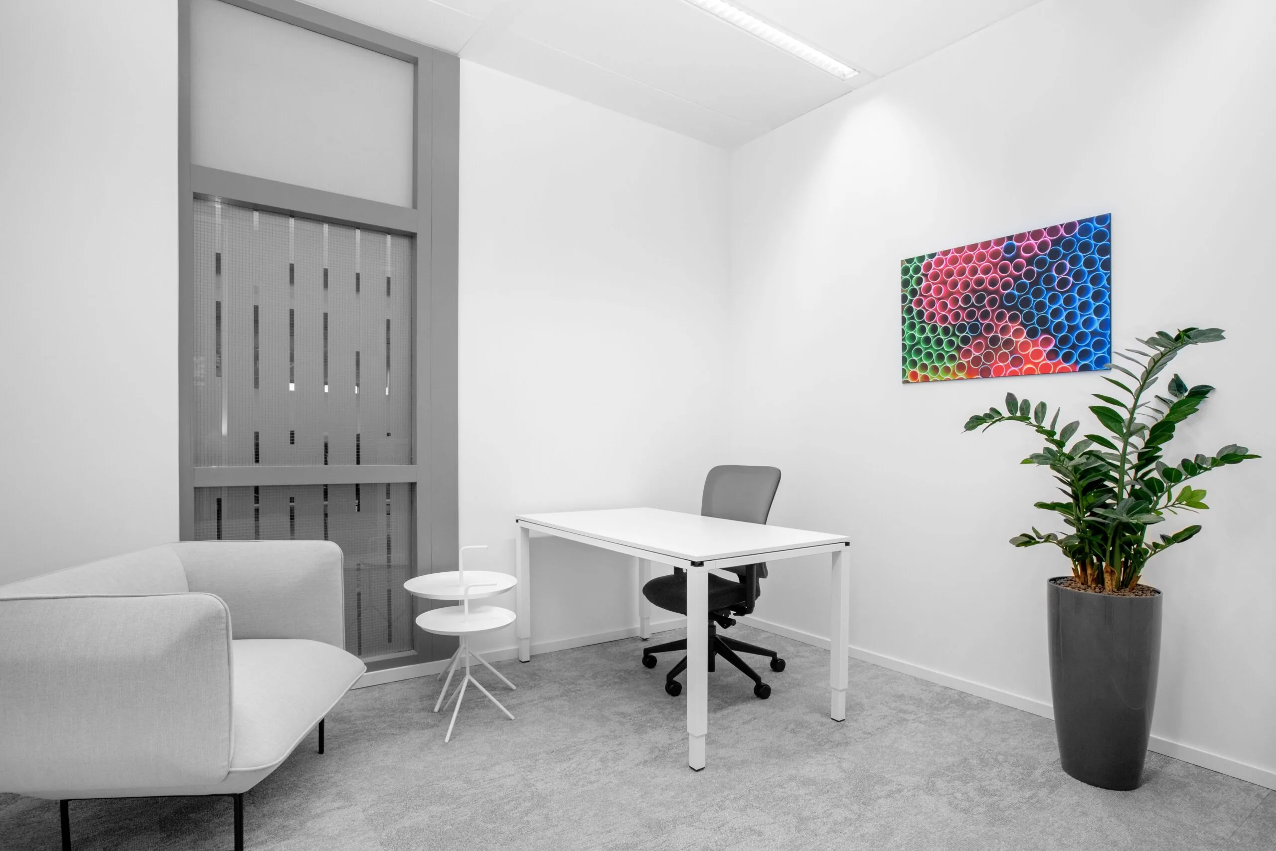 Moderne, lichte kantoorruimte aan de Laarderhoogtweg in Amsterdam met bureau, stoel, zitbank, plant en kleurrijk muurkunstwerk.