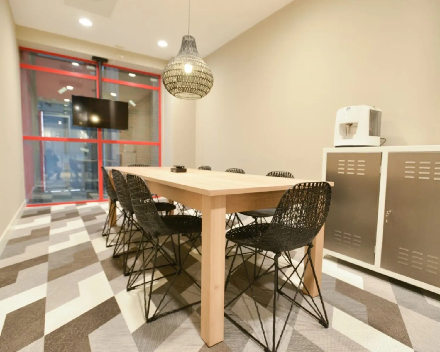Vergaderruimte in het Olympisch Stadion in Amsterdam met houten tafel, moderne zwarte stoelen en een flatscreen aan de wand.