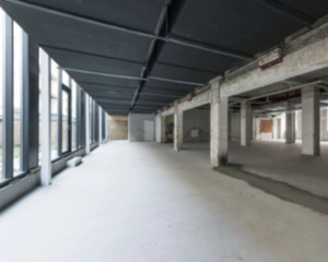 Leegstaande, industriële kantoorruimte aan de Karel du Jardinstraat 4 in Amsterdam met betonnen vloeren en grote ramen.