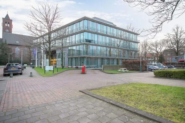 Modern kantoorgebouw met glazen gevel aan de Cuserstraat 91 in Amsterdam, omringd door parkeerplaatsen en groen.