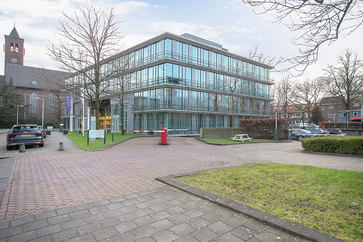 Modern kantoorgebouw met glazen gevel aan de Cuserstraat 91 in Amsterdam, omringd door parkeerplaatsen en groen.