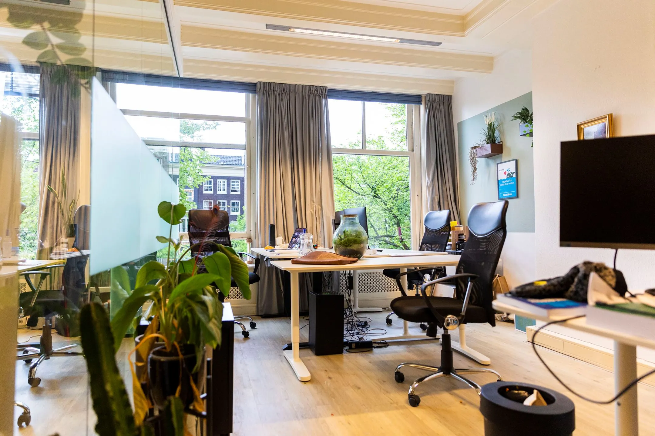 Moderne kantoorruimte aan het Singel in Amsterdam met werkplekken, planten en grote ramen met uitzicht op grachtenpanden.