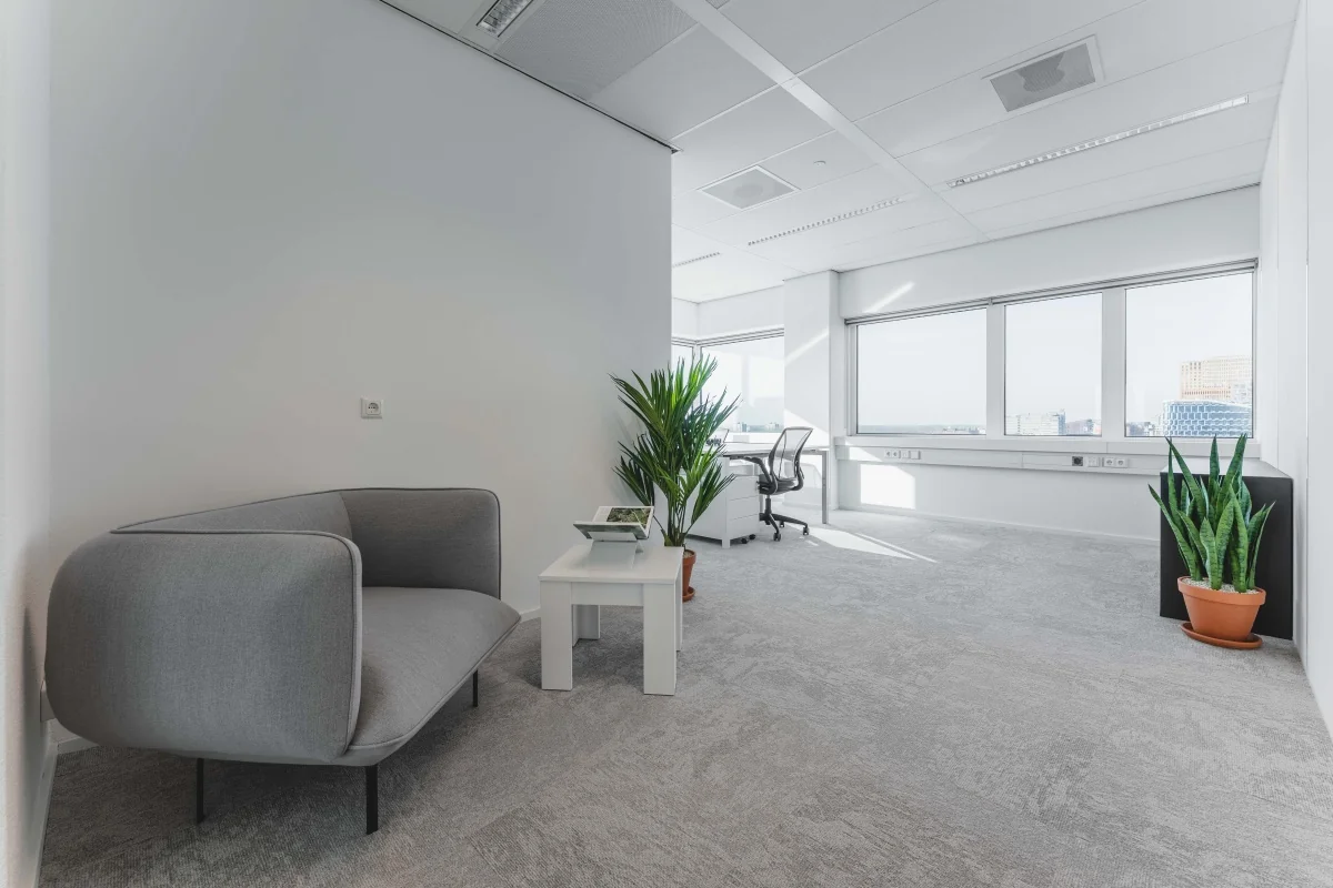 Een moderne en lichte kantoorruimte met een grijze bank, planten en een bureau bij de Barbara Strozzilaan 101 in Amsterdam.