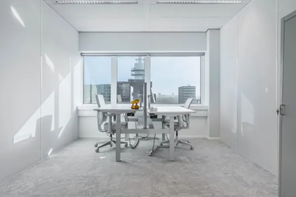 Moderne, lichte kantoorruimte met twee bureaus en stoelen bij een groot raam met uitzicht op de stad, gelegen aan de Barbara Strozzilaan 101 in Amsterdam.