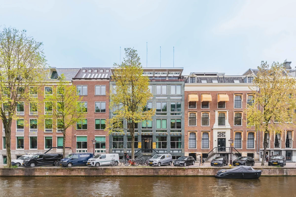 Gevels van historische panden aan de Herengracht in Amsterdam, met auto's geparkeerd langs de kade.