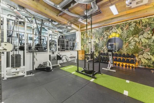 Een moderne fitnessruimte met diverse trainingsapparaten en een plantenmotief op de muur.