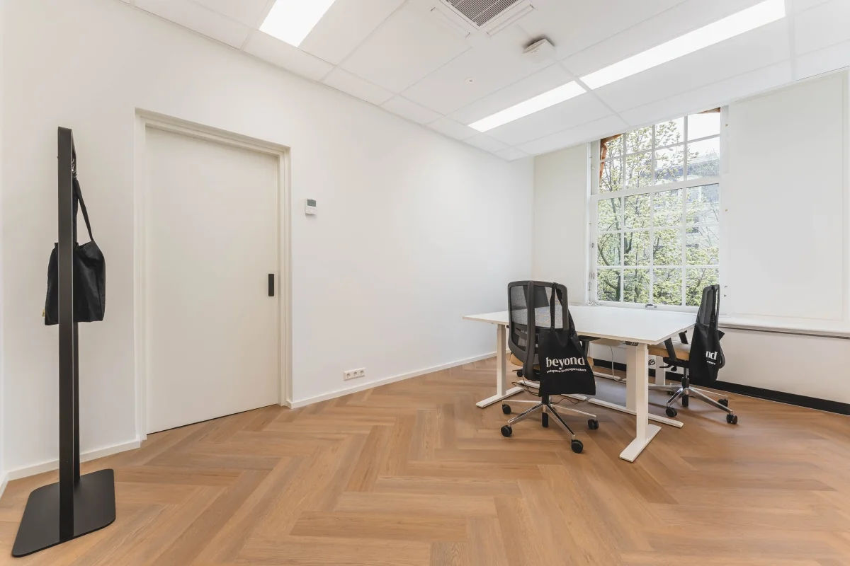 Lichte kantoorruimte aan de Herengracht 471 in Amsterdam met houten vloer, bureaus en stoelen.