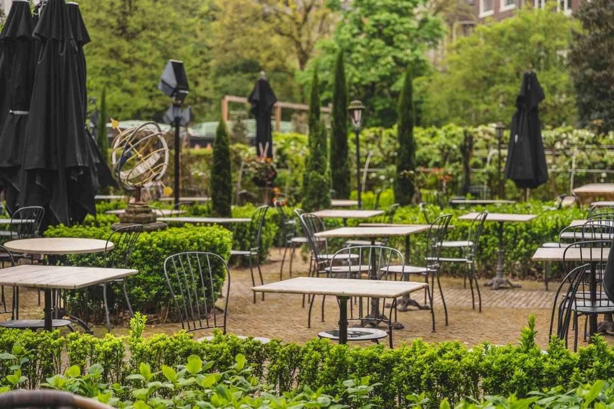 Terras met lege tafels en stoelen omringd door weelderig groen in Amsterdam.