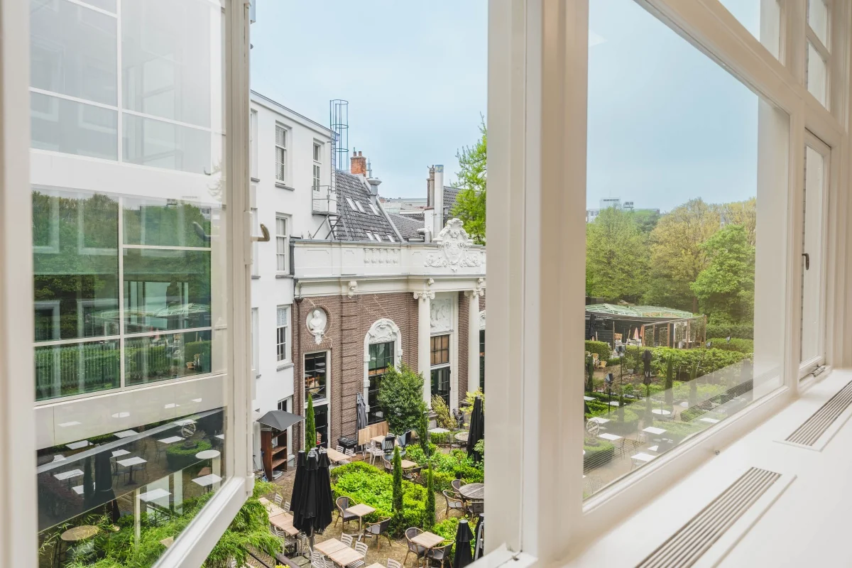 Uitzicht vanaf een raam op een groene binnentuin en klassiek gebouw aan de Herengracht in Amsterdam.