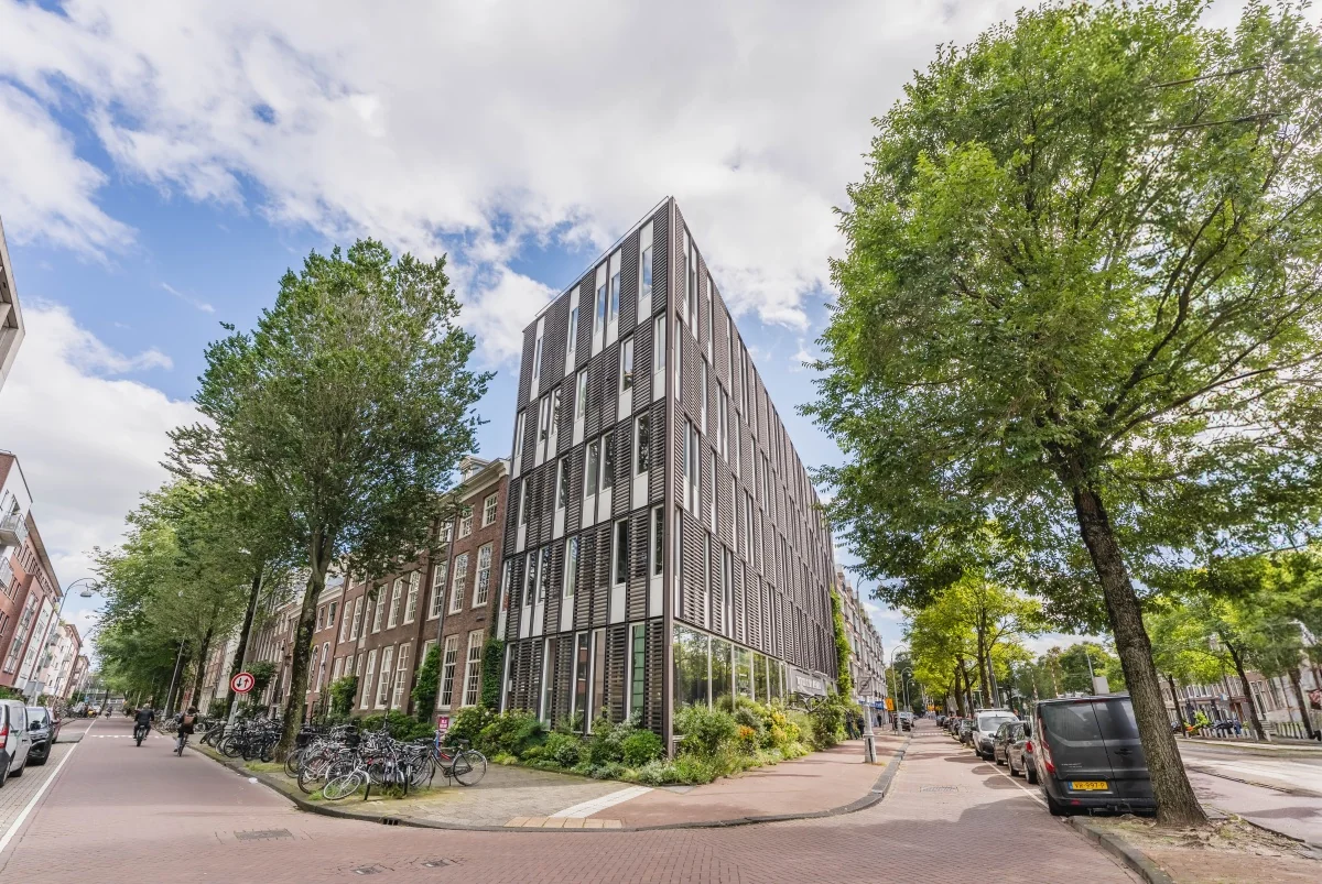 Een modern kantoorgebouw op de hoek van een straat in Amsterdam met bomen en geparkeerde fietsen.