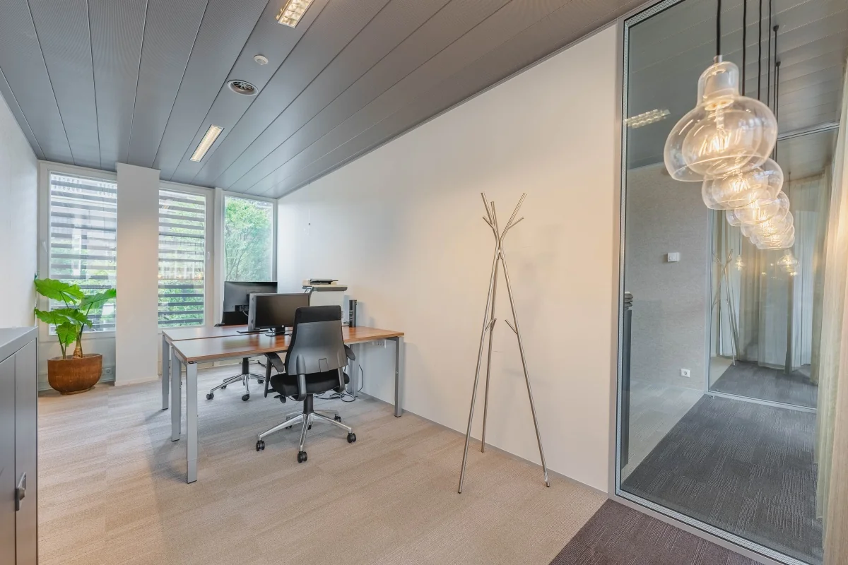 Een moderne en lichte kantoorruimte met bureaus, stoelen, een plant en glazen panelen aan de Muiderstraat in Amsterdam.