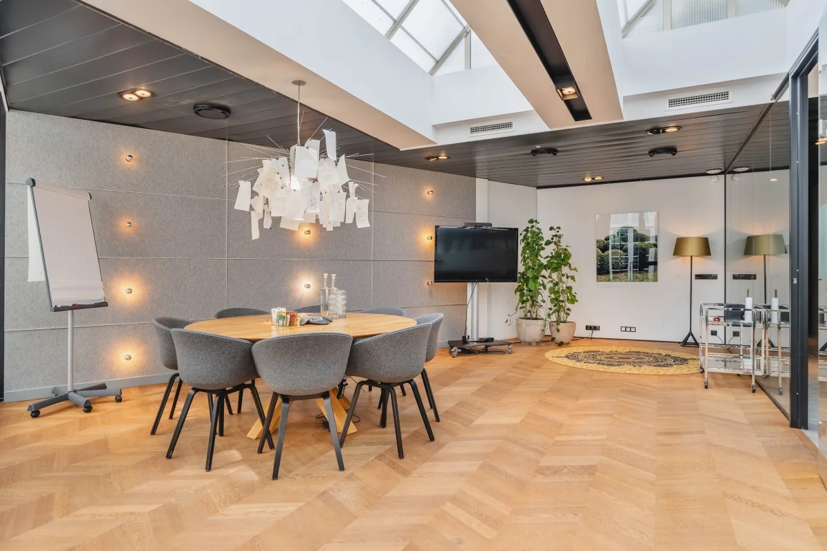 Moderne vergaderruimte met glazen dak, houten vloer, ronde tafel en stoelen in Amsterdam, Muiderstraat.