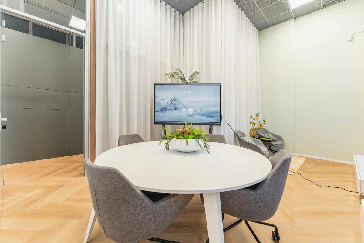 Moderne vergaderruimte aan de Weesperstraat in Amsterdam met ronde tafel, grijze stoelen, flatscreen en decoratieve planten.
