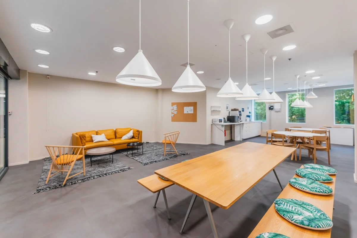 Een moderne kantoorruimte met een gele bank, houten tafels en een kitchenette.