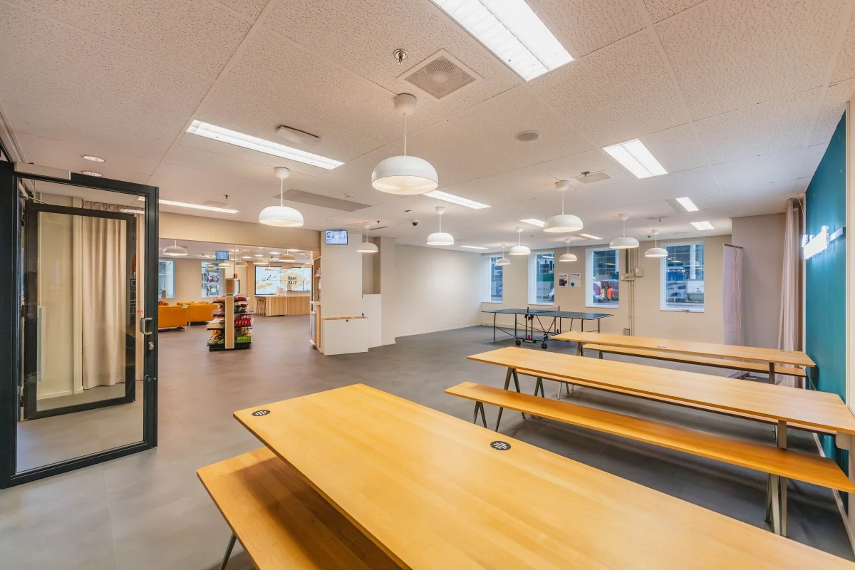 Een moderne kantoorruimte met lange houten tafels, hanglampen en een pingpongtafel in een open ruimte.