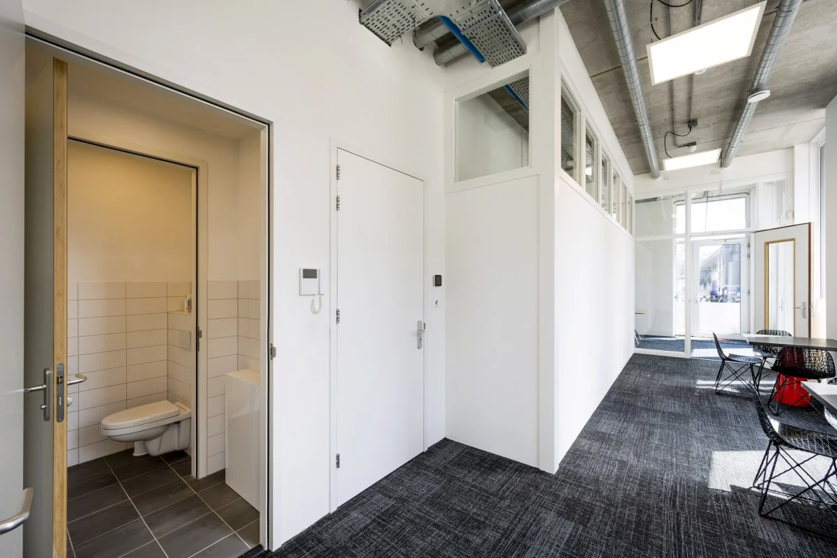 Moderne kantoorruimte met openstaande deur naar toilet en kantoor, minimalistische inrichting.