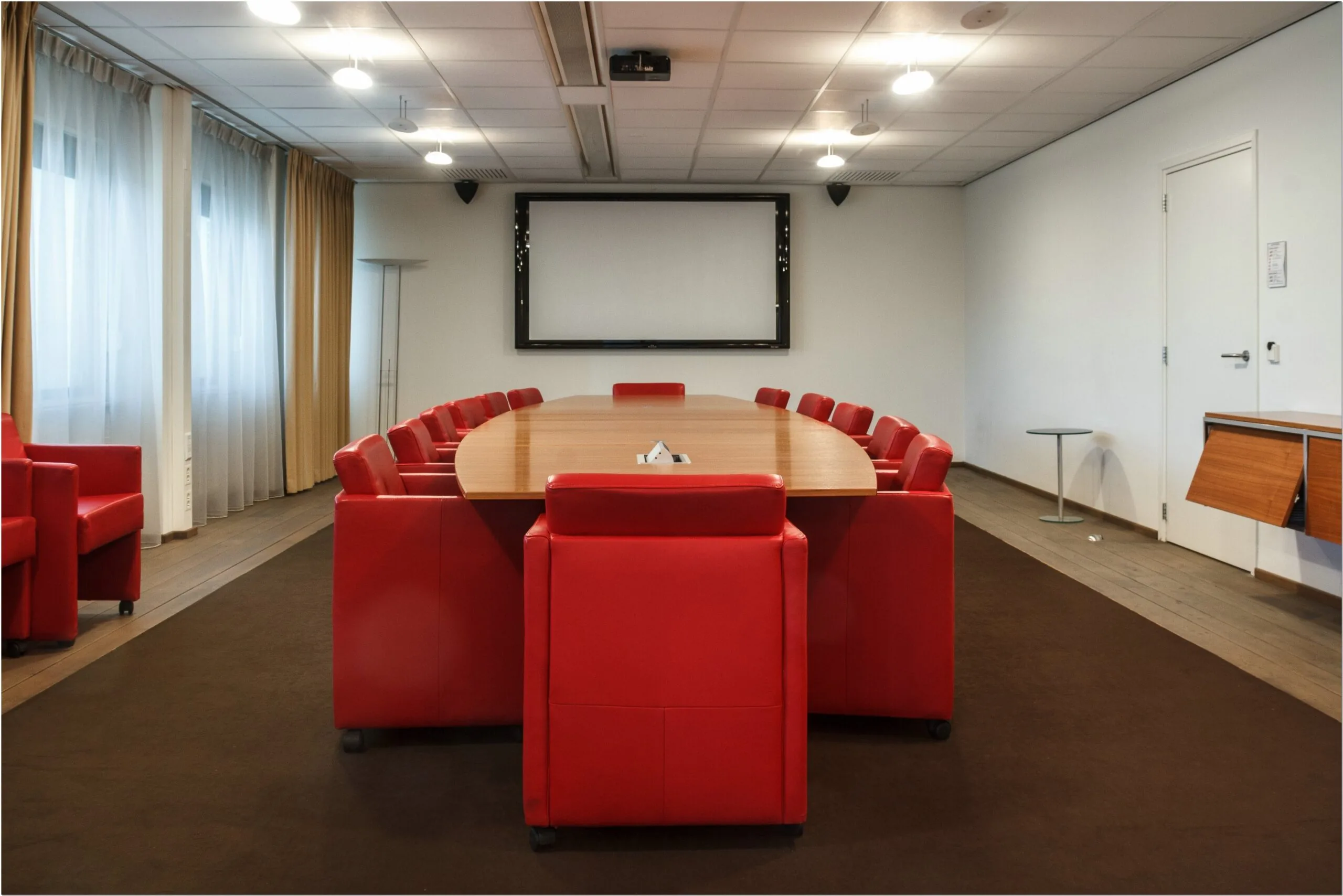 Vergaderruimte met grote ovale tafel, rode stoelen en een presentatiescherm in kantoor Bredewater 26 Zoetermeer.