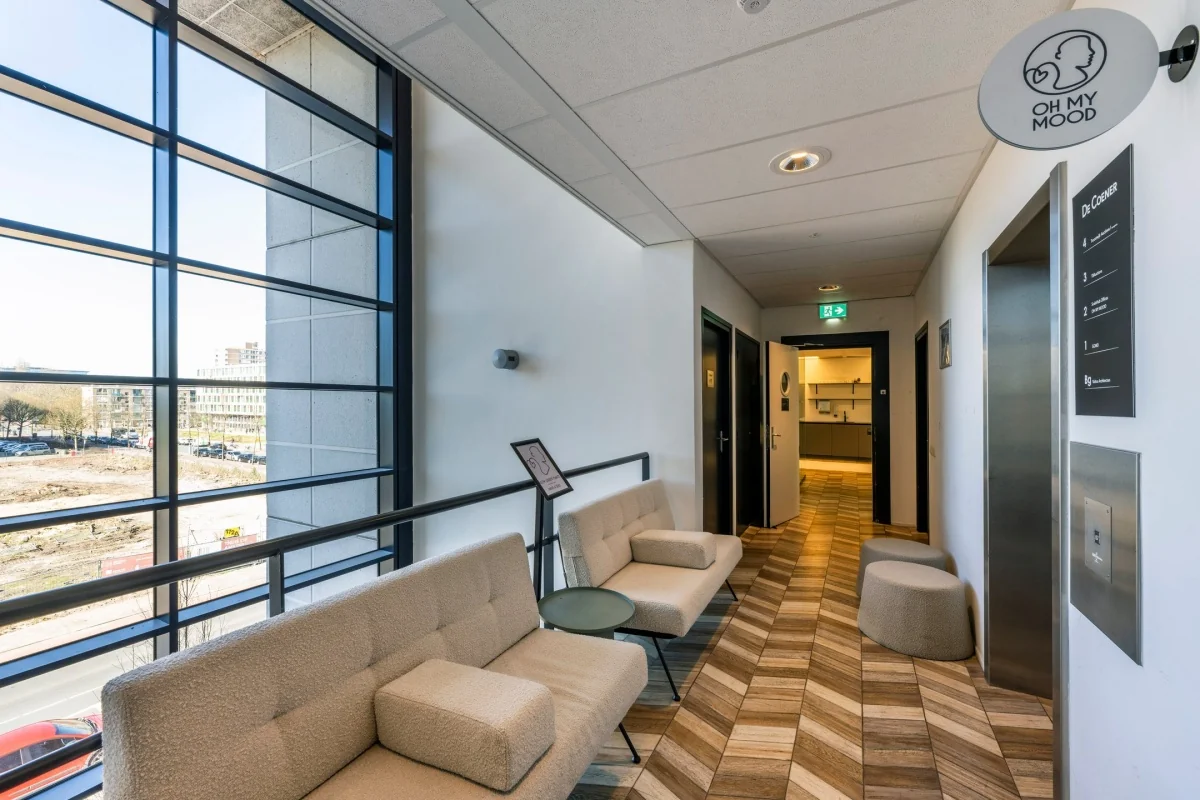 De gang van een moderne kantoorruimte met grote ramen, comfortabele banken en een lift bij Overscheistraat 59 in Amsterdam.