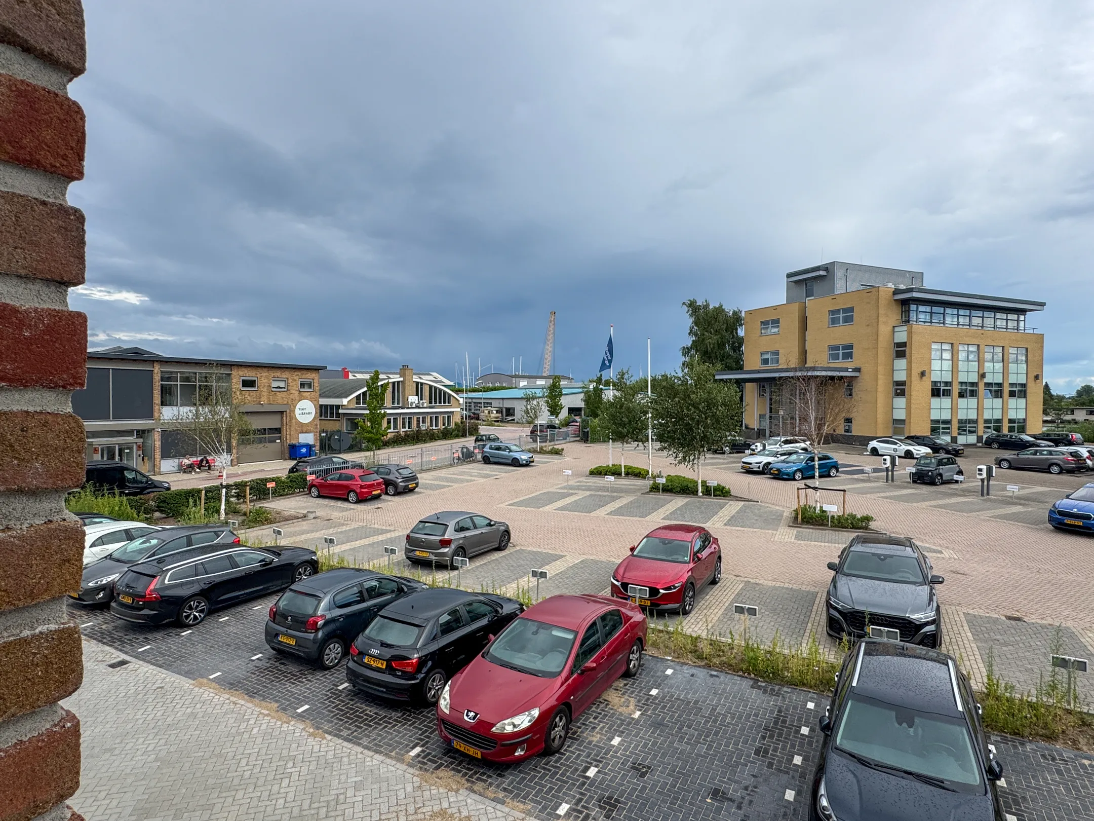 View of the office buildings and parking lot at Nijverheidslaan 10 in Weesp, with several parked cars under a cloudy sky.