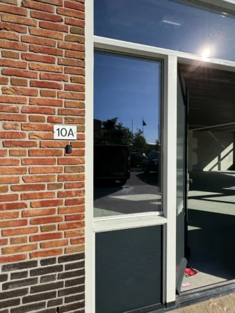 Entrance of office space at Nijverheidslaan 10A in Weesp with a partially open glass door and visible brick wall.