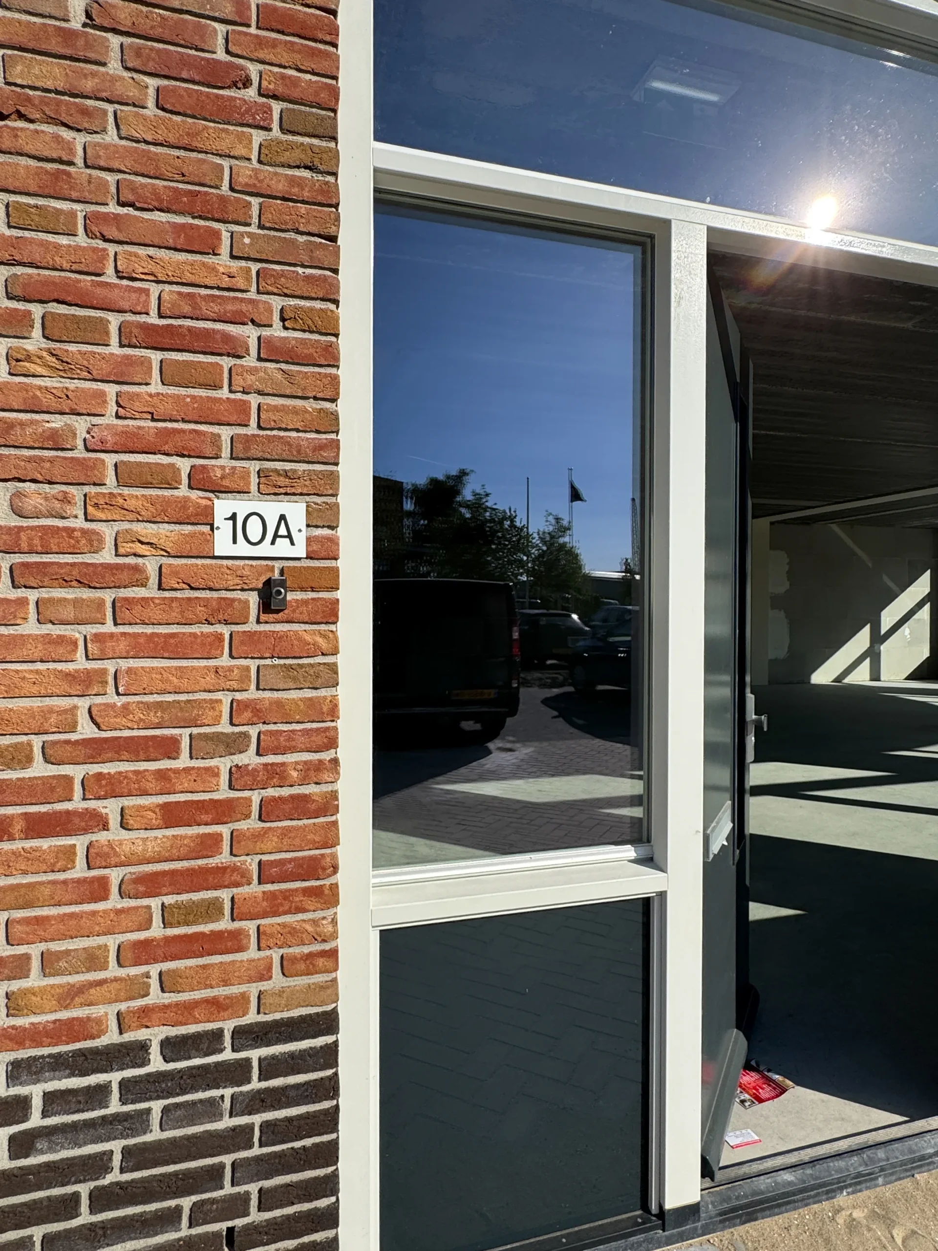 Entrance of office space at Nijverheidslaan 10A in Weesp with a partially open glass door and visible brick wall.