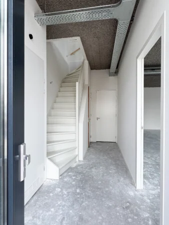 Interior view of a modern office space at Nijverheidslaan 10 in Weesp, featuring a white staircase and unfinished concrete floor.