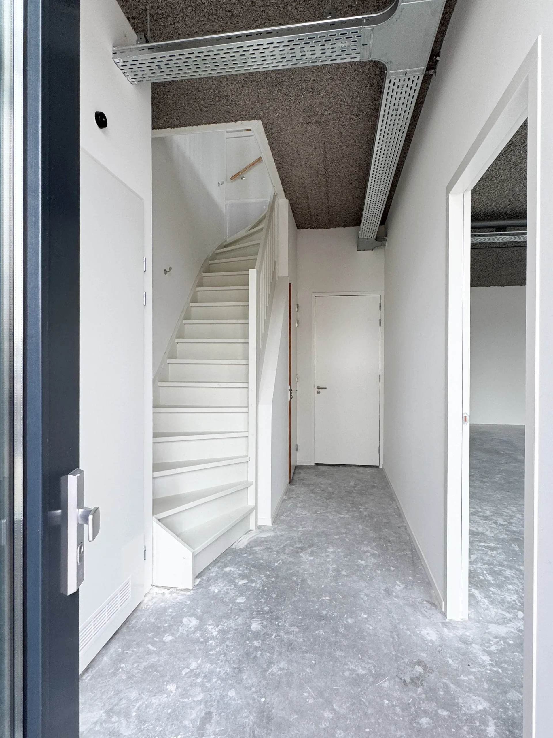 Interior view of a modern office space at Nijverheidslaan 10 in Weesp, featuring a white staircase and unfinished concrete floor.