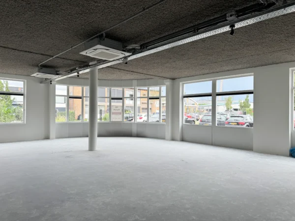 Empty office space for rent at Nijverheidslaan 10 in Weesp, with large windows and a view of the parking area.