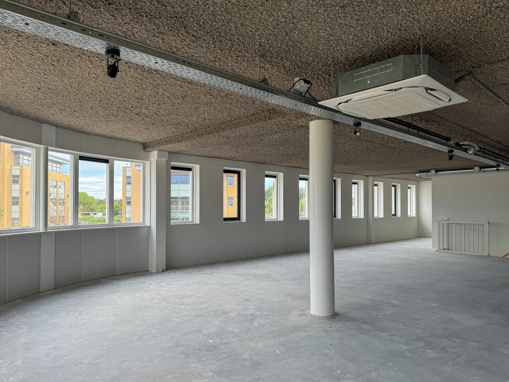 Modern, empty office space for rent at Nijverheidslaan 10 in Weesp, featuring large windows and an industrial ceiling design.