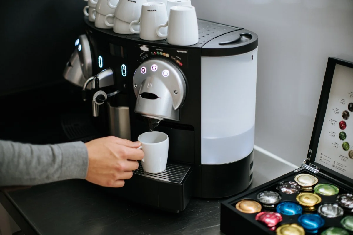 Persoon maakt koffie met een Nespresso-apparaat bij Keizersgracht 64, met een capsulehouder op het aanrecht.
