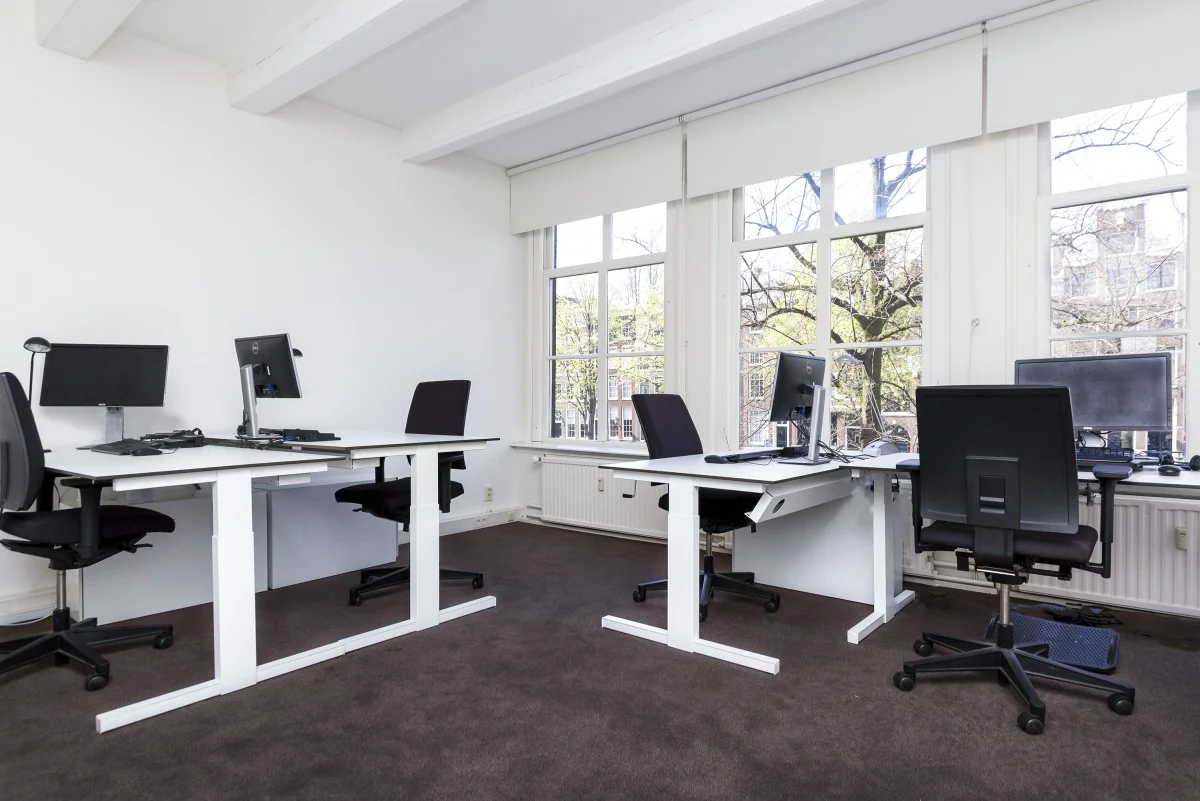 Modern kantoorinterieur op Keizersgracht 64 met vier werkplekken en grote ramen met uitzicht op de gracht.