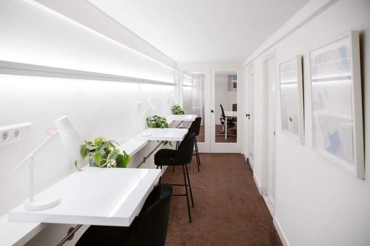 Lichte, moderne werkruimte met witte bureaus, zwarte stoelen en kamerplanten in Keizersgracht 64.