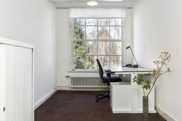 Kleine, lichte kantoorruimte aan de Keizersgracht 64 met bureau bij een groot raam en minimalistische inrichting.