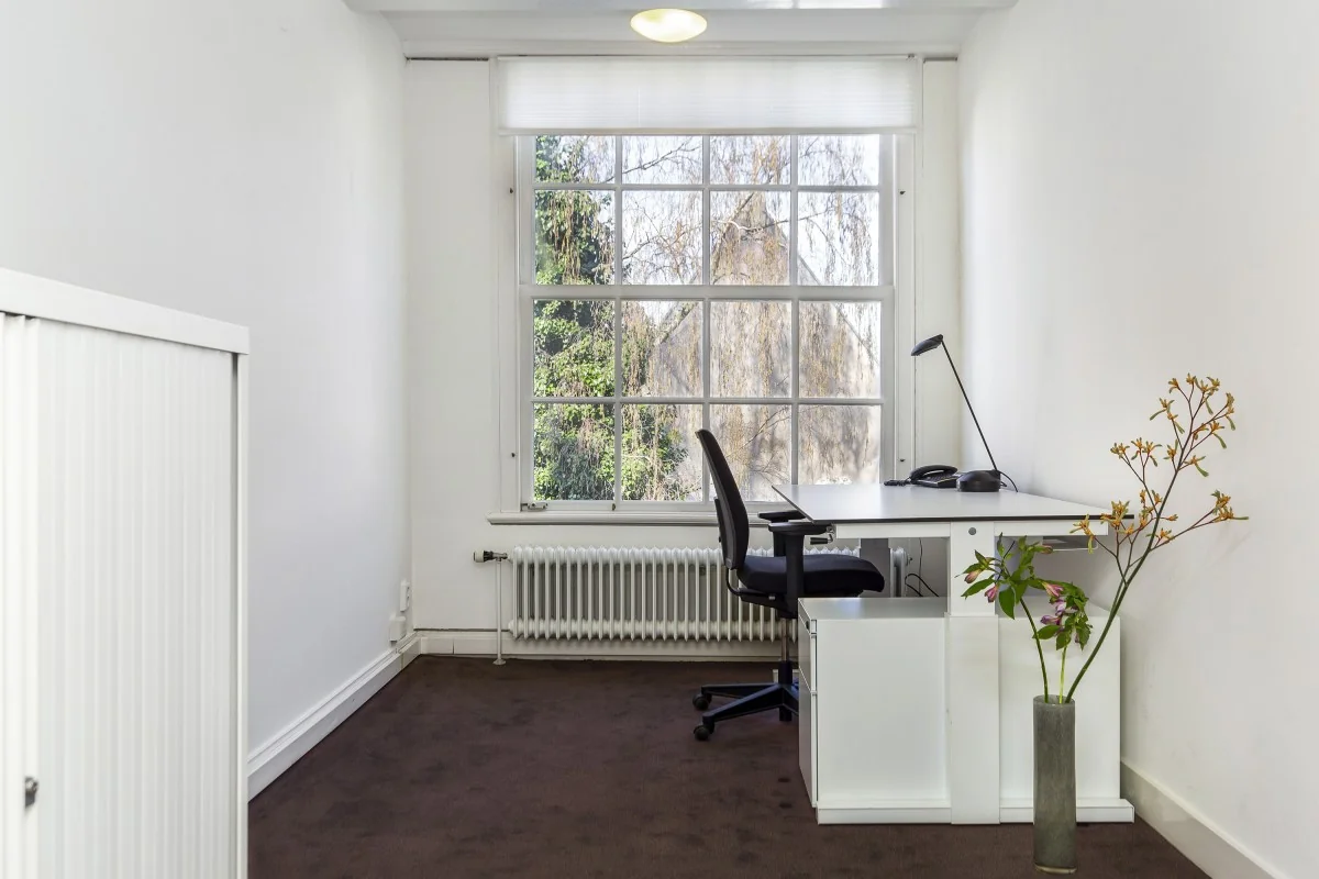 Kleine, lichte kantoorruimte aan de Keizersgracht 64 met bureau bij een groot raam en minimalistische inrichting.