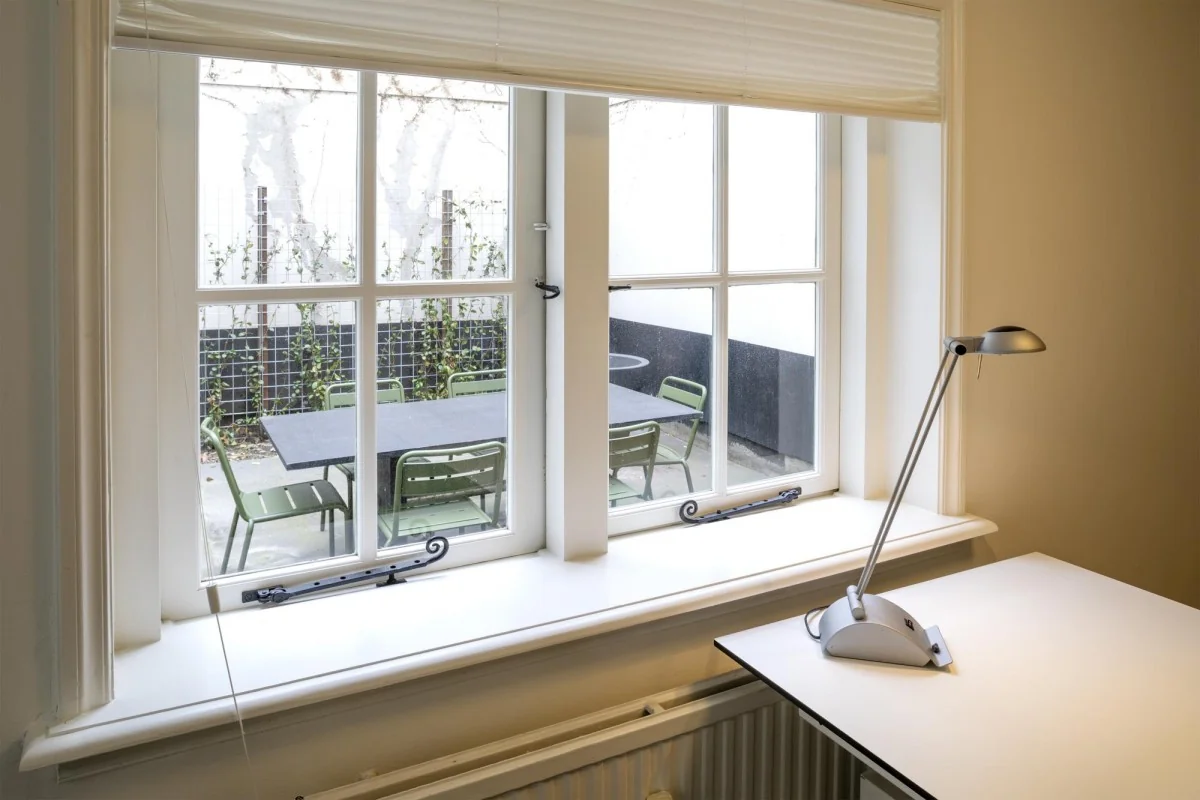 Uitzicht vanuit een kamer op Keizersgracht 97 op een binnentuin met een zwarte buitentafel en groene stoelen.