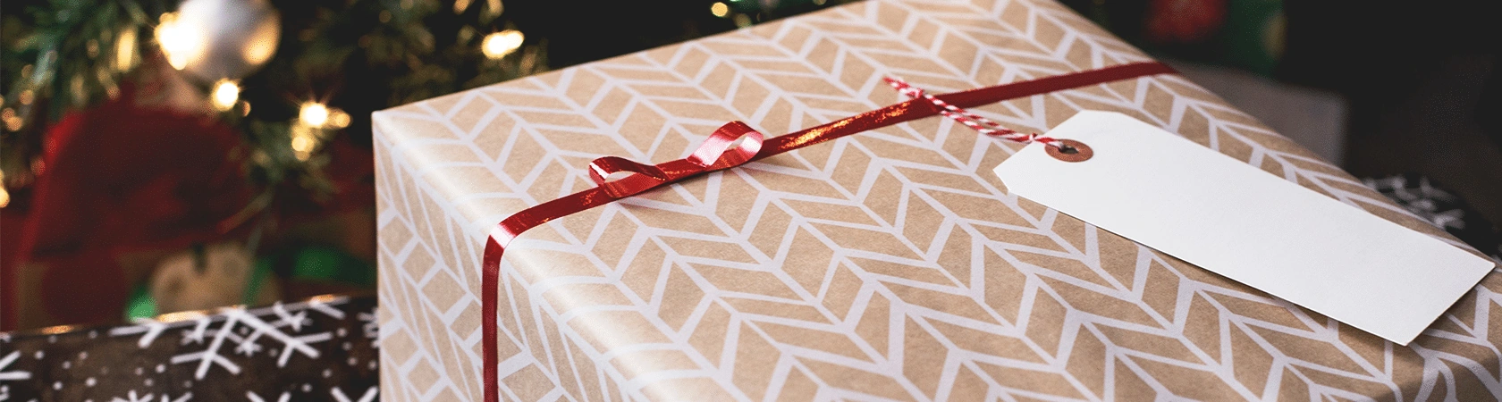 Een persoonlijk kerstpakket met rood lint en naamlabel onder de kerstboom.