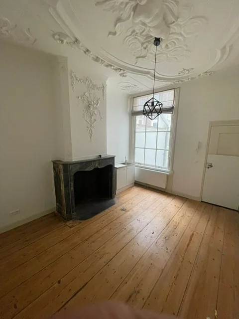 Klassieke kamer in Kloveniersburgwal 56 met houten vloer, sierlijke plafondornamenten en een marmeren schouw.