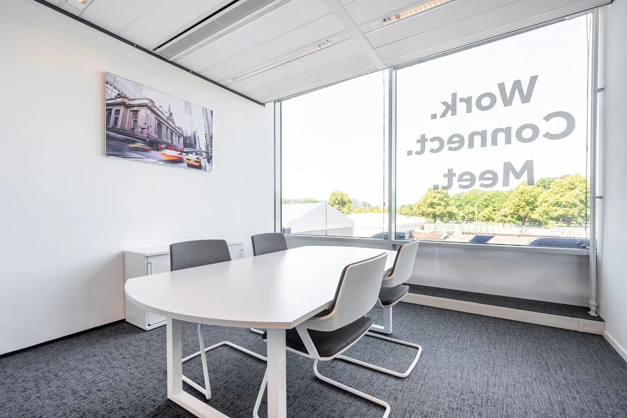 Moderne vergaderruimte aan het Koningin Julianaplein met witte tafel, grijze stoelen en groot raam met de tekst "Work. Connect. Meet."