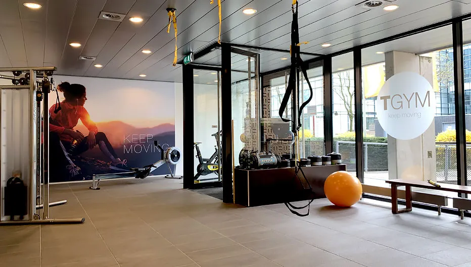 Moderne fitnessruimte bij TGYM aan de Laan van Vredenoord 33 met fitnessapparatuur, een oranje oefenbal en grote ramen.