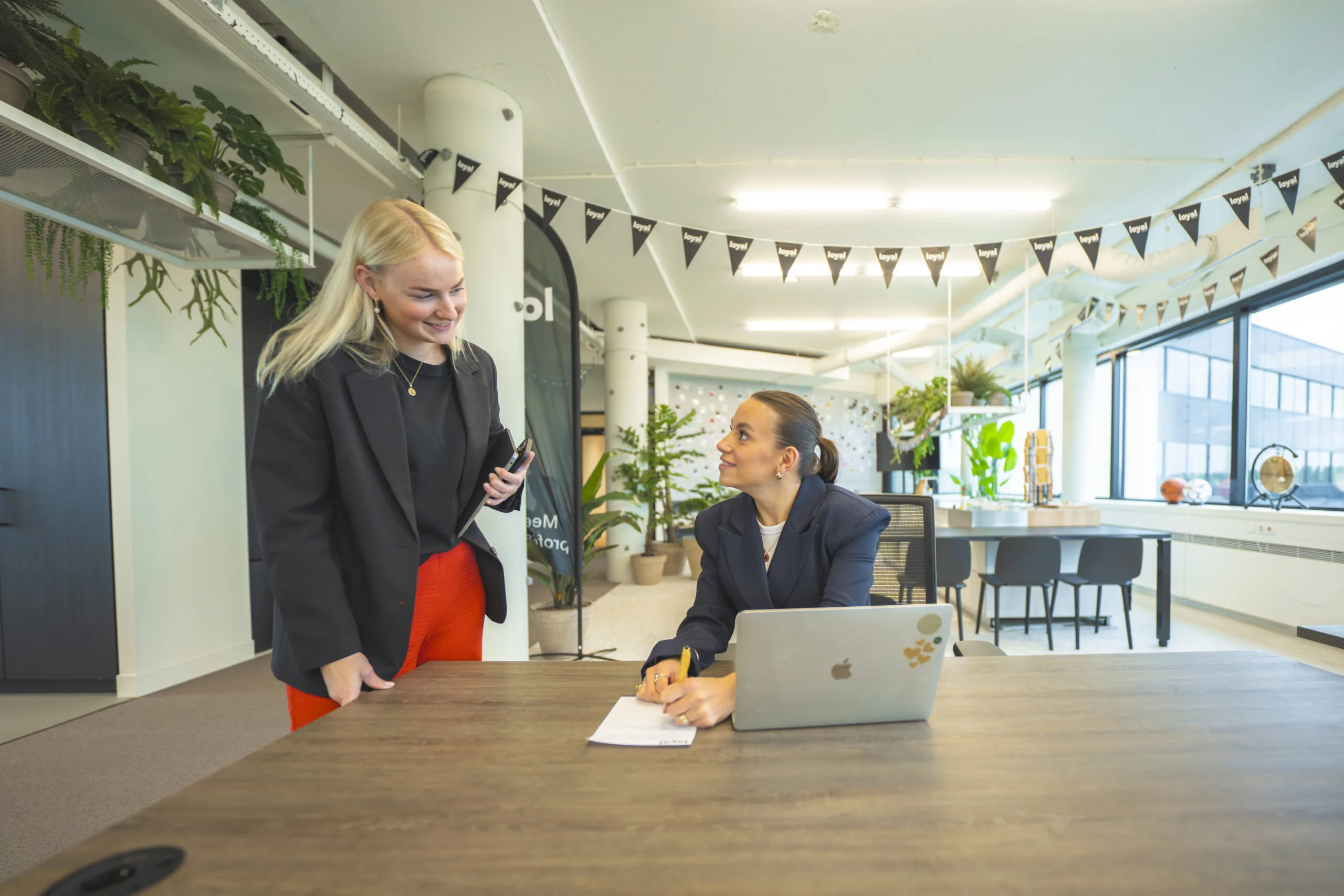 Twee zakelijk geklede vrouwen overleggen bij een bureau in een modern ingericht kantoor van Loyal Interim.