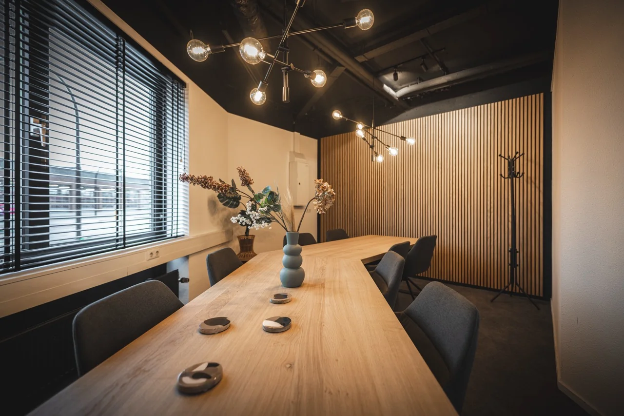 Vergaderruimte Felix met een grote houten tafel, moderne verlichting en een houten lattenwand, zonder mensen.